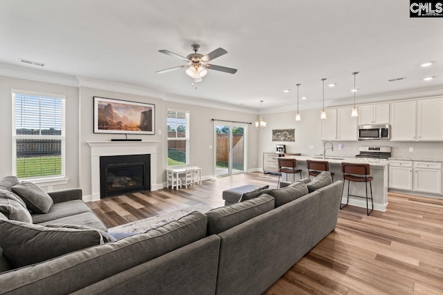 living area with light wood-style flooring, a glass covered fireplace, recessed lighting, ceiling fan, and ornamental molding