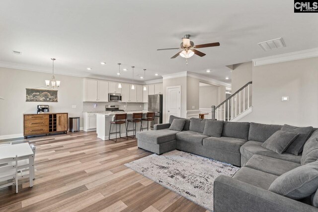 living area with crown molding, ceiling fan with notable chandelier, light wood-type flooring, and recessed lighting