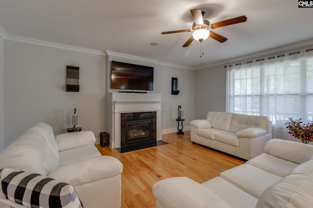 living area featuring a fireplace with flush hearth, ornamental molding, light wood-type flooring, baseboards, and ceiling fan