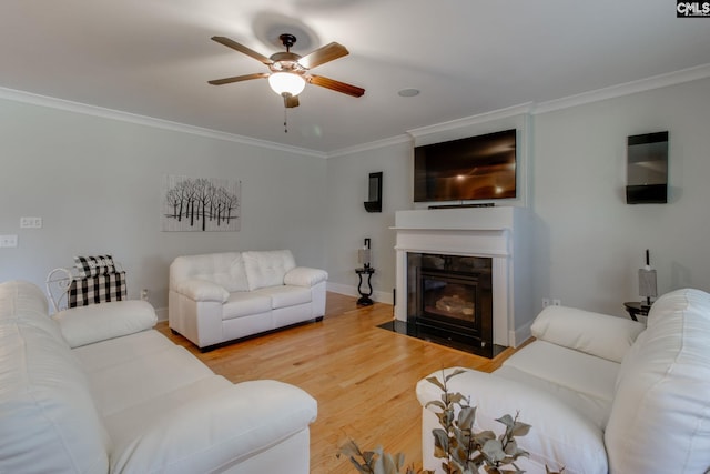living area with a fireplace with flush hearth, a ceiling fan, crown molding, and light wood-type flooring