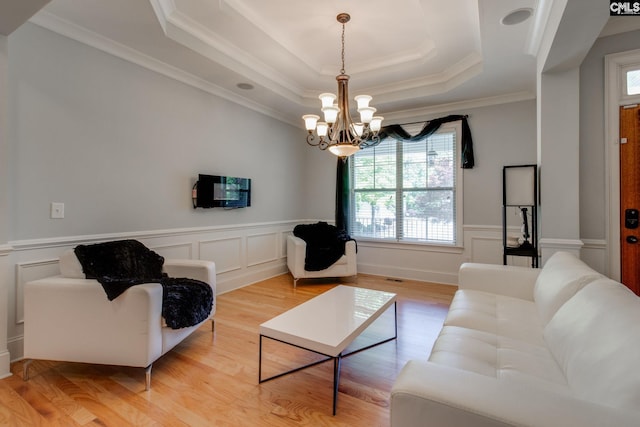 living room featuring a wainscoted wall, an inviting chandelier, a tray ceiling, crown molding, and light wood-style flooring