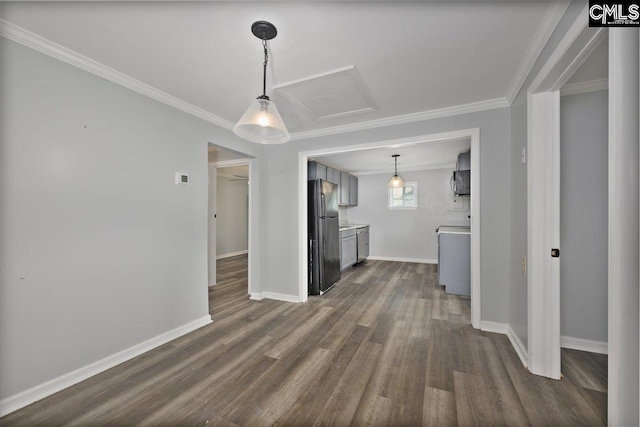 unfurnished dining area featuring dark wood finished floors, baseboards, attic access, and ornamental molding