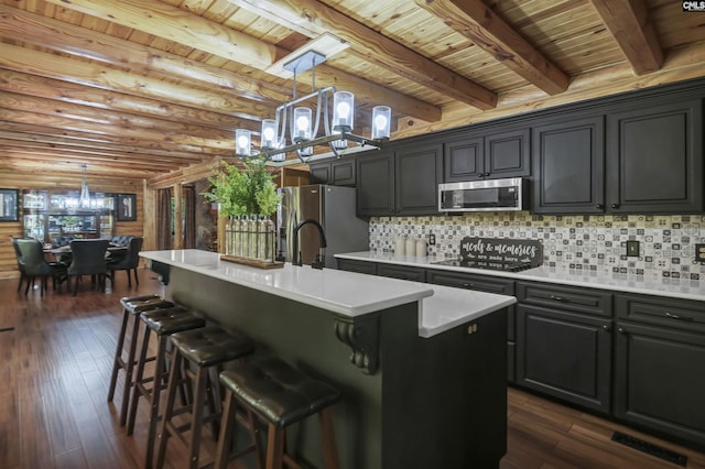 kitchen with an inviting chandelier, light countertops, a kitchen island with sink, appliances with stainless steel finishes, and dark wood-style flooring