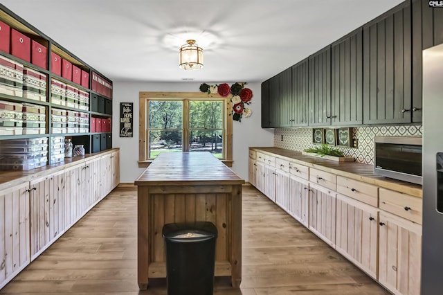 kitchen featuring stainless steel microwave, light wood-type flooring, a kitchen island, decorative backsplash, and butcher block countertops