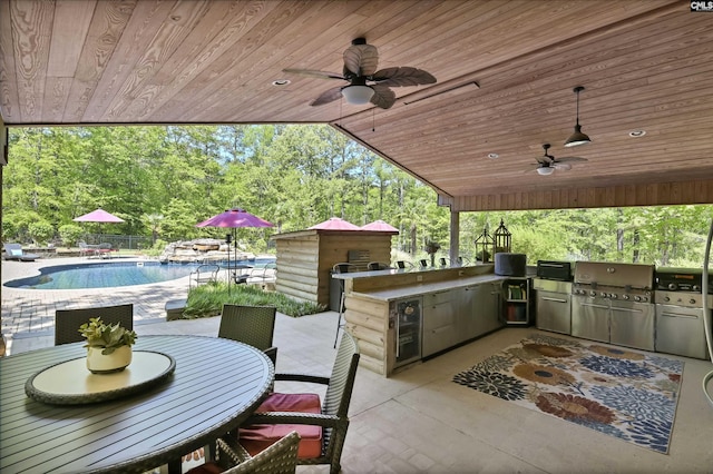 view of patio / terrace with exterior kitchen, a ceiling fan, outdoor dining space, and an outdoor pool