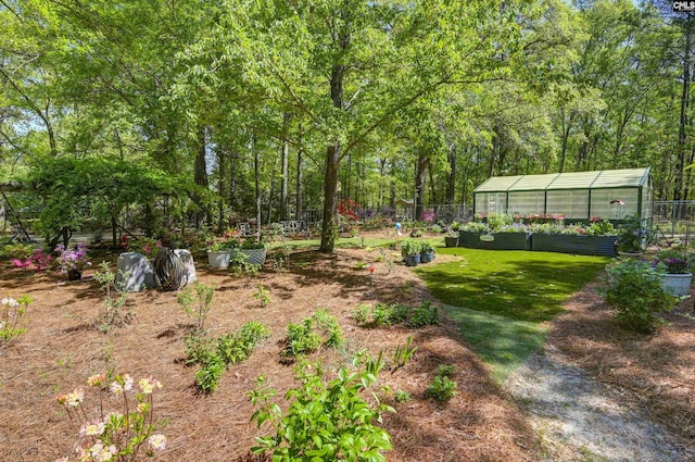 view of yard with a vegetable garden, fence, an outbuilding, and a greenhouse