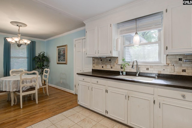 kitchen with white cabinets, a sink, tasteful backsplash, dark countertops, and a chandelier