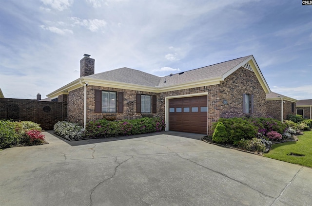 ranch-style home with concrete driveway, a chimney, a shingled roof, an attached garage, and brick siding