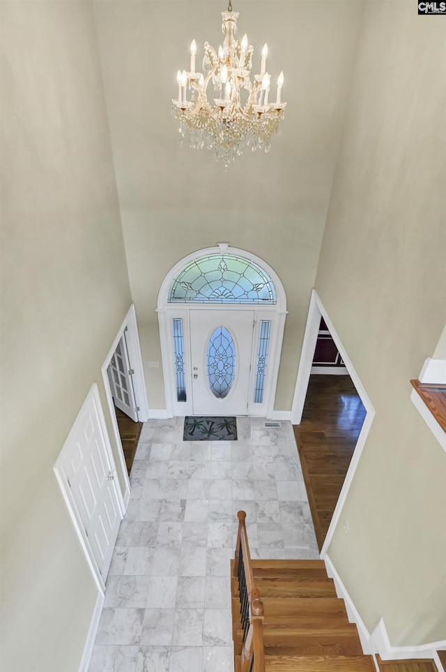 foyer entrance with marble finish floor, a high ceiling, a notable chandelier, and baseboards