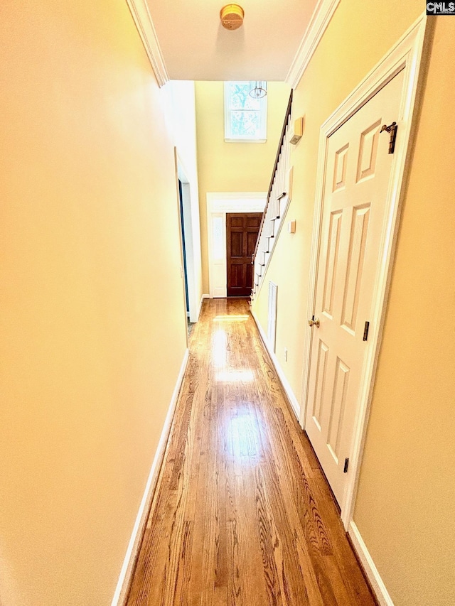 hallway with light wood finished floors, baseboards, stairs, and ornamental molding