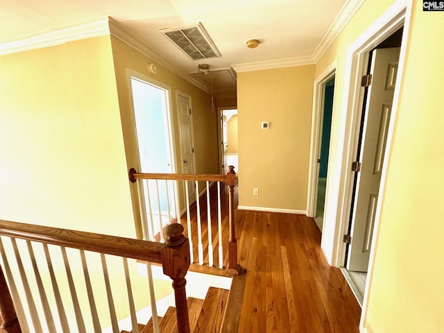 hallway featuring wood finished floors, visible vents, an upstairs landing, crown molding, and baseboards