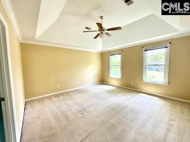 carpeted empty room with a raised ceiling, visible vents, crown molding, and ceiling fan