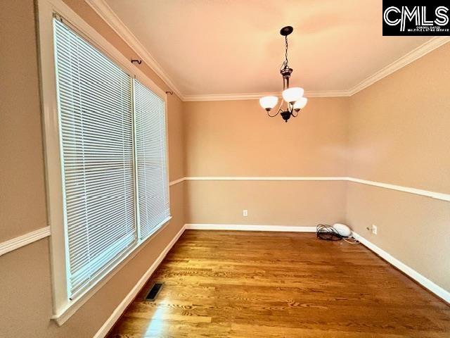 unfurnished dining area featuring wood finished floors, visible vents, ornamental molding, baseboards, and a chandelier