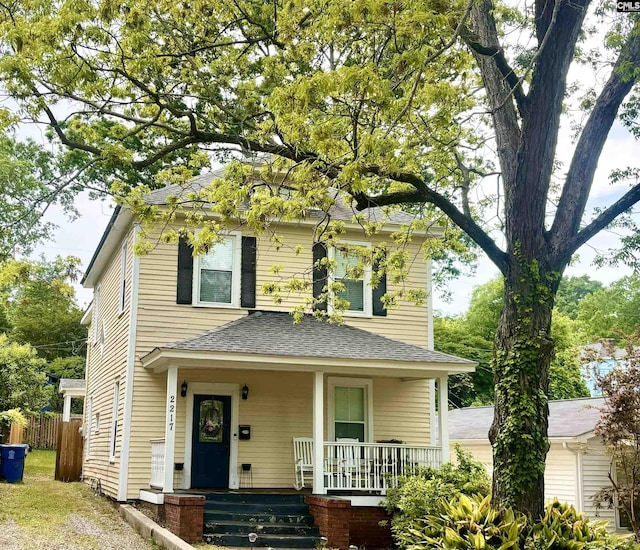 traditional style home with roof with shingles, fence, and covered porch