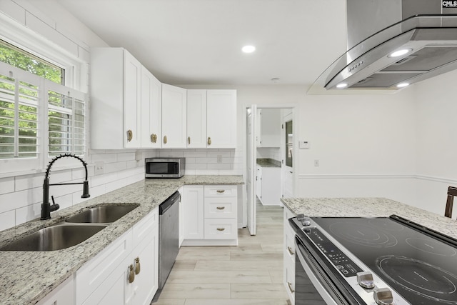 kitchen featuring wall chimney exhaust hood, white cabinetry, stainless steel appliances, and a sink
