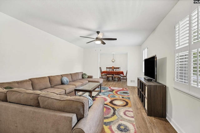 living area featuring light wood finished floors, baseboards, a wealth of natural light, and ceiling fan