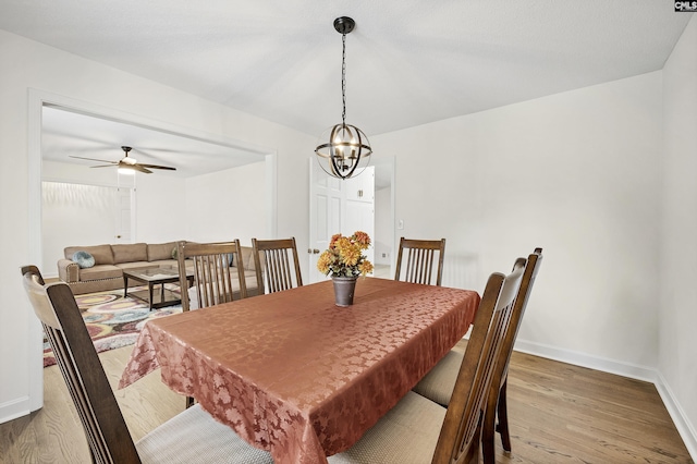 dining space featuring baseboards, wood finished floors, and ceiling fan with notable chandelier