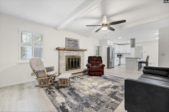 living room with a ceiling fan, crown molding, beamed ceiling, light wood-style flooring, and a brick fireplace