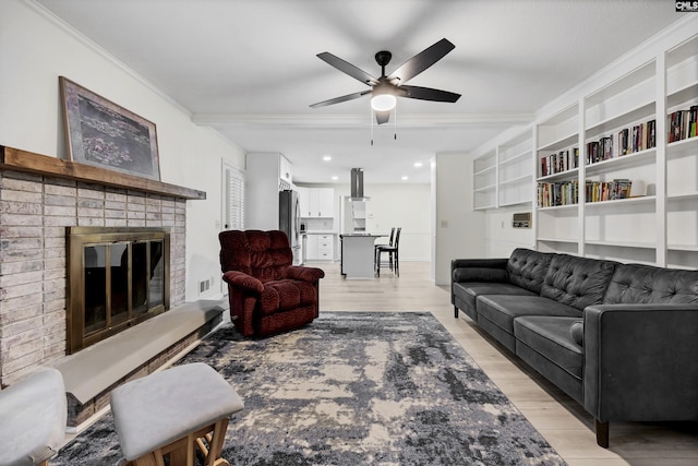 living area featuring a ceiling fan, crown molding, light wood-style floors, a brick fireplace, and visible vents