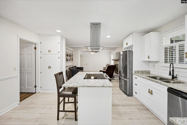 kitchen with light wood finished floors, a center island, a kitchen breakfast bar, a sink, and appliances with stainless steel finishes