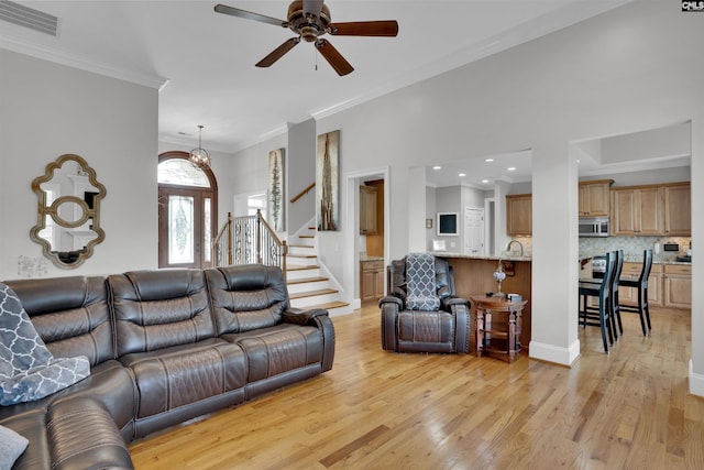 living room with ceiling fan, light wood-type flooring, crown molding, stairs, and visible vents