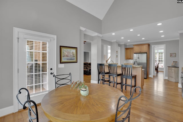 dining space featuring crown molding, light wood-type flooring, lofted ceiling, and baseboards