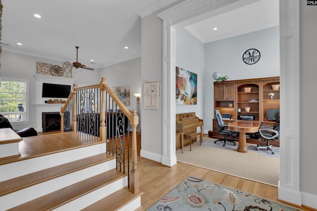stairway featuring a fireplace, a ceiling fan, baseboards, ornamental molding, and wood finished floors
