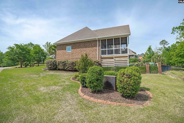 view of home's exterior with brick siding, a shingled roof, a sunroom, and a lawn