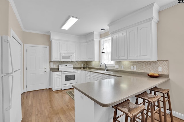 kitchen with white appliances, a breakfast bar, a sink, white cabinetry, and a peninsula