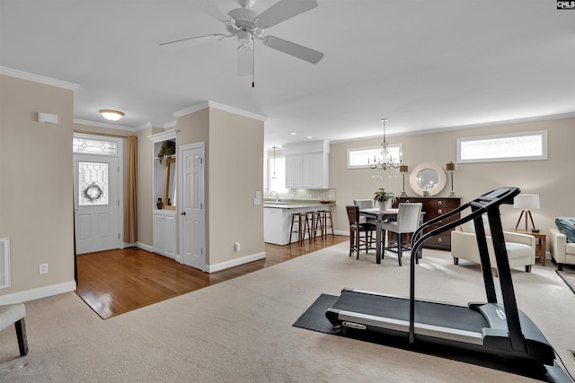 workout area featuring ornamental molding, ceiling fan with notable chandelier, carpet flooring, a sink, and baseboards