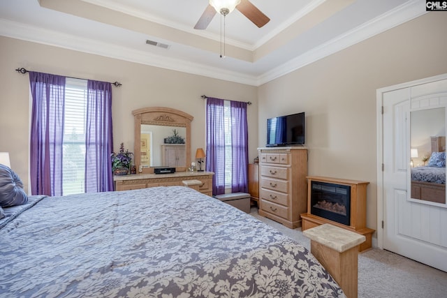 bedroom featuring crown molding, light colored carpet, a raised ceiling, visible vents, and a glass covered fireplace