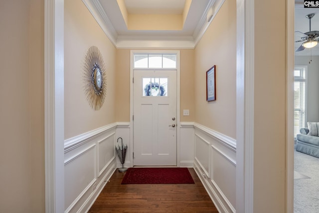 entryway with dark wood-style floors, ceiling fan, crown molding, a wainscoted wall, and a decorative wall