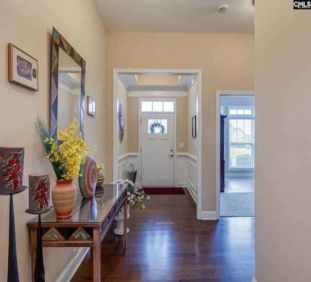 entrance foyer with dark wood-style flooring, a wainscoted wall, ornamental molding, and a tray ceiling