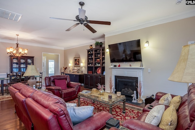 living area featuring visible vents, a glass covered fireplace, ornamental molding, wood finished floors, and ceiling fan with notable chandelier