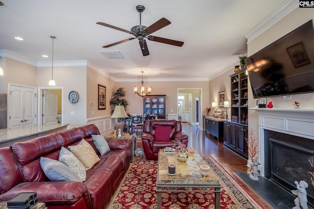 living area with crown molding, ceiling fan with notable chandelier, visible vents, a fireplace with flush hearth, and dark wood-type flooring