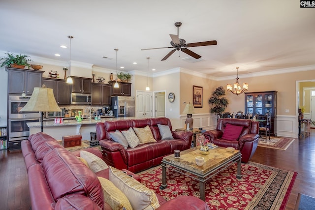 living area with crown molding, a wainscoted wall, recessed lighting, dark wood finished floors, and ceiling fan with notable chandelier
