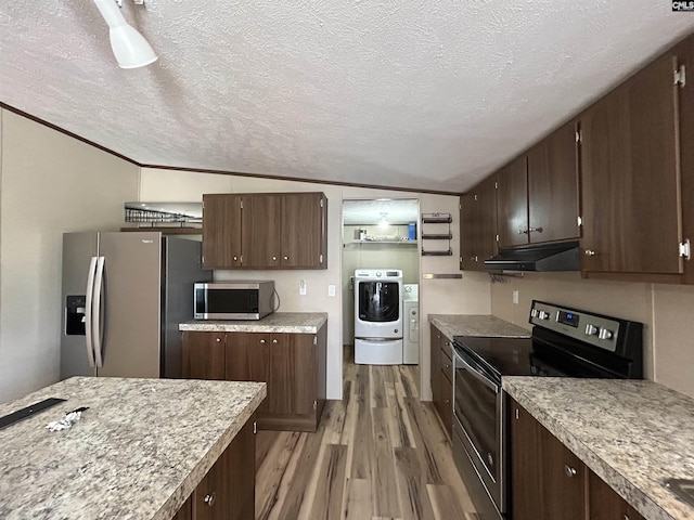 kitchen with under cabinet range hood, washer / dryer, a textured ceiling, appliances with stainless steel finishes, and wood finished floors