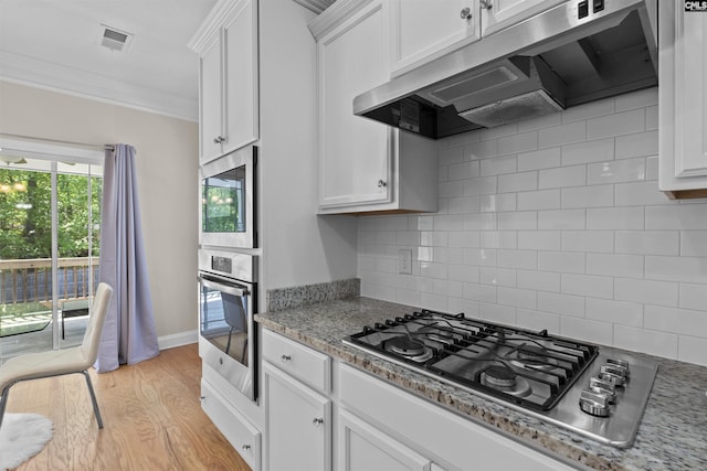 kitchen featuring under cabinet range hood, crown molding, backsplash, white cabinets, and appliances with stainless steel finishes