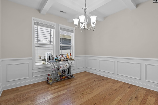 unfurnished dining area featuring visible vents, a chandelier, beam ceiling, light wood finished floors, and wainscoting