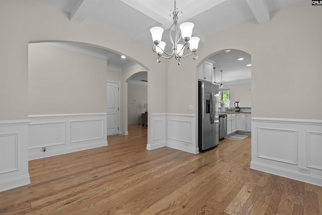 unfurnished dining area featuring beam ceiling, light wood-type flooring, a notable chandelier, and arched walkways