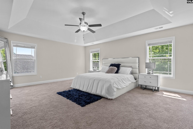 carpeted bedroom with a raised ceiling, a ceiling fan, visible vents, and baseboards