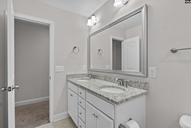 full bath with toilet, double vanity, a sink, and baseboards