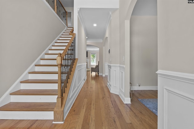 stairs with crown molding, recessed lighting, arched walkways, and hardwood / wood-style floors