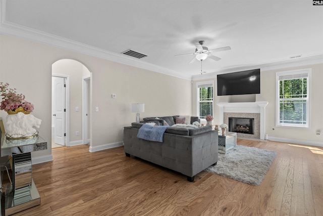 living area with crown molding, light wood-style floors, visible vents, ceiling fan, and arched walkways