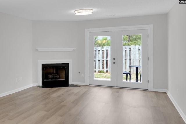 unfurnished living room featuring french doors, a fireplace with flush hearth, wood finished floors, and baseboards