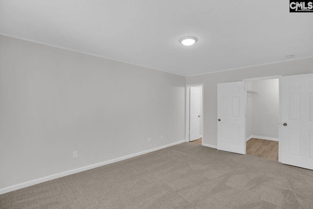 unfurnished bedroom featuring baseboards, a spacious closet, ornamental molding, and carpet