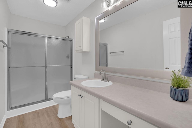 bathroom with vanity, wood finished floors, toilet, and a stall shower