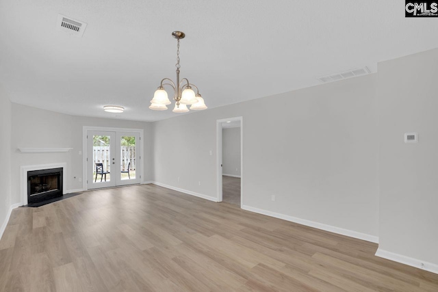 unfurnished living room with a notable chandelier, visible vents, light wood-style flooring, and baseboards