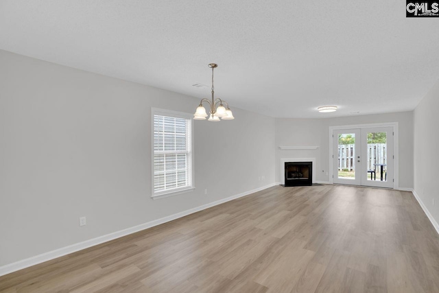 unfurnished living room with light wood finished floors, a fireplace with flush hearth, a notable chandelier, baseboards, and french doors