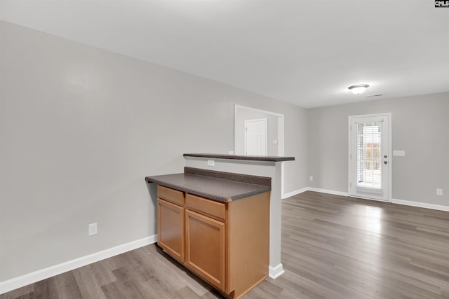 kitchen featuring wood finished floors, dark countertops, a peninsula, and baseboards
